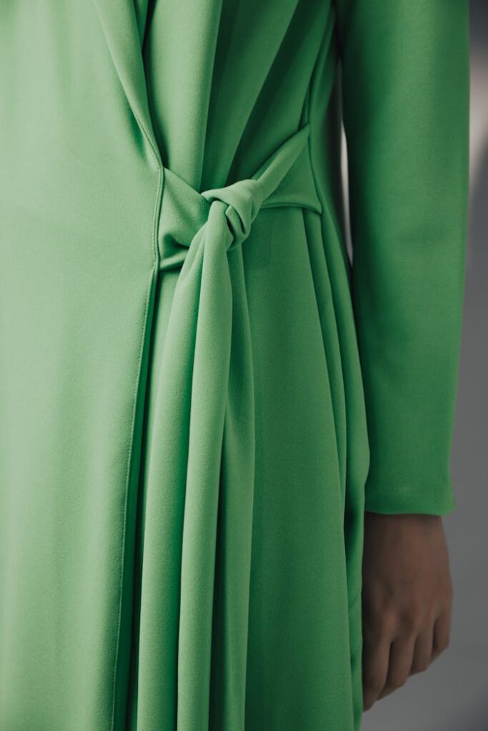 Close-up of a woman's green dress with a tied belt, showcasing fashion design.