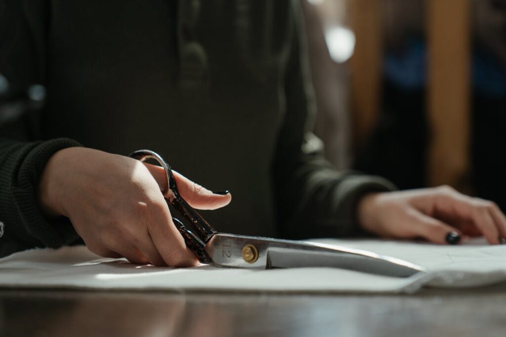 Close-up of a tailor's hands cutting fabric with scissors, emphasizing craftsmanship and skill.